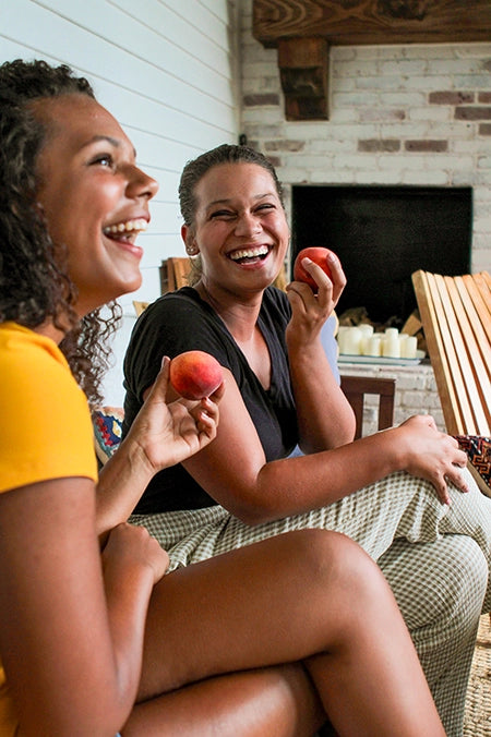 Two women laughing together while eating peaches