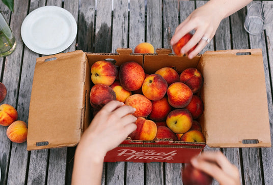 People reaching into a box to grab peaches for themselves