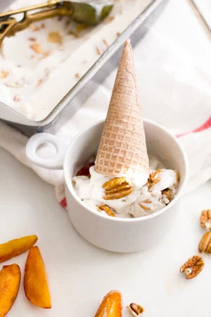 An upside down peach ice cream cone in a dish topped with pecans