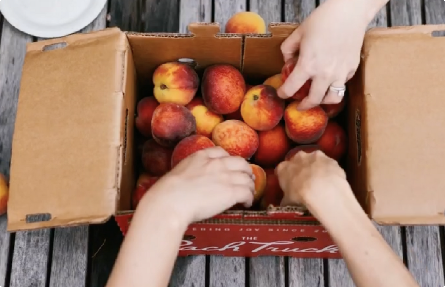 People reaching into a box to get peaches