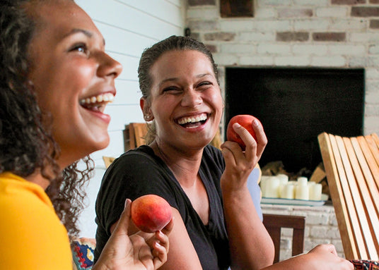 Two women laughing together while eating peaches
