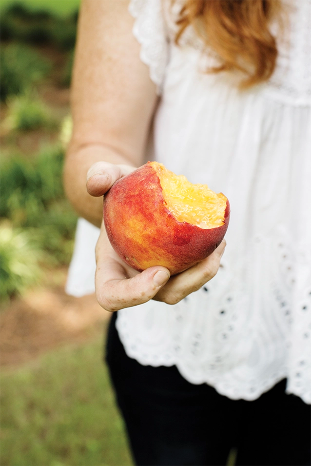 Woman holding a bitten peach out in one hand